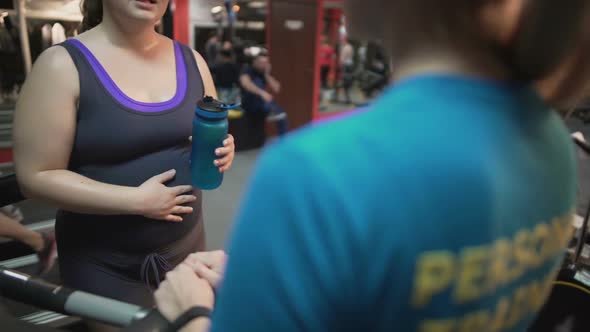 Pregnant Woman Consulting With Personal Trainer on Pregnancy Exercises in Gym