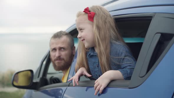 Beautiful Little Daughter Sticking Out of Car Window Talking with Father Admiring Beauty of Nature