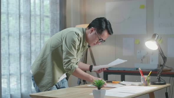 Side View Of Asian Man Designer Is Arranging The Layout Bond On The Table At The Office