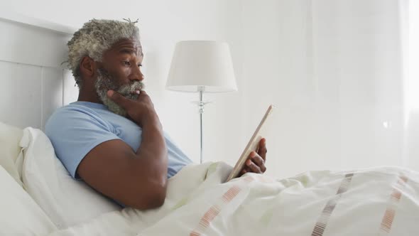 Senior man using digital tablet in bed at home