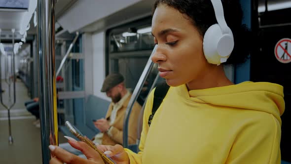 Young Girl Standing in Metro Train Wearing Headphones and Looking in Her Phone