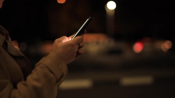 Woman Is Chatting in the Smartphone Against the Background of the Evening City