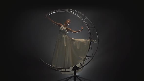 Woman Gymnast in White Dress Rotates on a Construction a Month. Smoke Background. Slow Motion