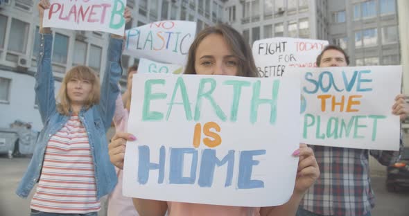 Portrait of Woman Holding Earth Is Home Poster and Looking at Camera. Female Protester Standing with