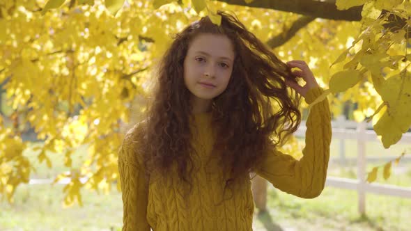 Pretty Caucasian Girl with Long Curly Hair Standing on the Background of Yellow Leaves. Redhead