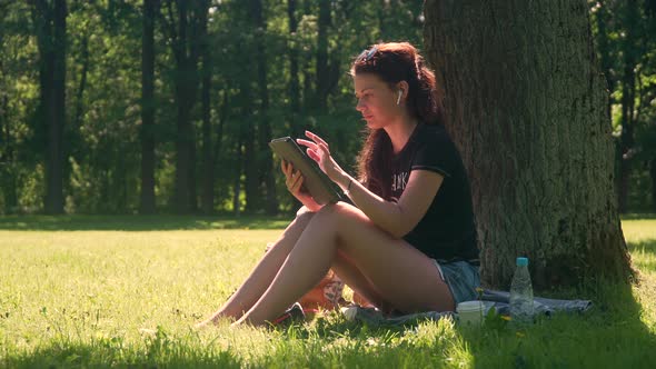 Young Woman In Park Uses Digital Tablet