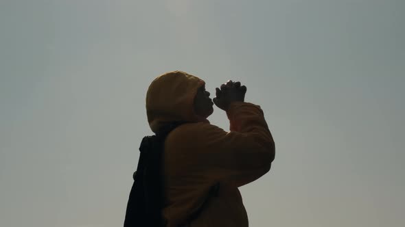 Silhouette of woman closed her eyes, praying on top of a mountain during sunset.