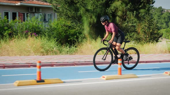 Athletic sportswoman in cycling sportswear and black helmet cycling on bike along bicycle lane path