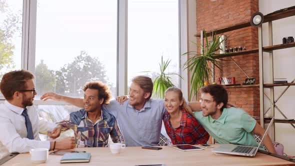 Interracial Males and Female Sitting at Table with Mobile Phones Tablets Laptop Hugging Each Other