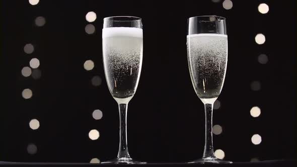 Two Transparent Glass of Chilled Sparkling Wine. Bokeh Blinking Black Background