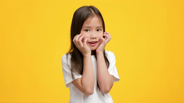 Funny Little Japanese Girl Posing Touching Face Over Yellow Background