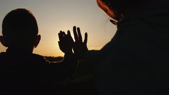 Silhouette Mom with Son Stretches Their Hands To the Sun