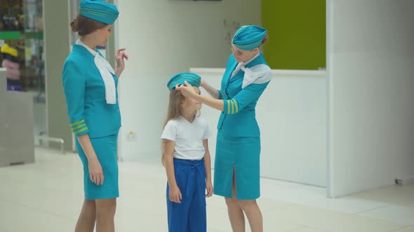 Smiling Young Woman Putting Stewardess Hat on Head of Pretty Little Girl. Portrait of Professional