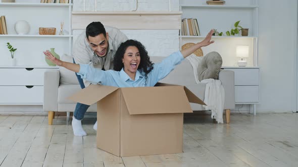 Hispanic Man Caring Loving Husband Boyfriend Pushing Large Cardboard Box with Beloved Wife