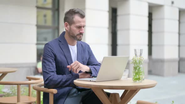 Man Thinking While Using Laptop Sitting in Outdoor Cafe