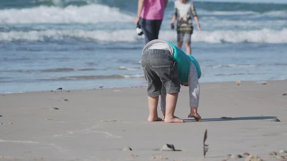 Toddler Boy in Waistcoat Is Playing with Sand on Sea Side.