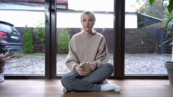 Frustrated Depressed Teenage Girl Sitting with Toy at Floor to Ceiling Window Thinking