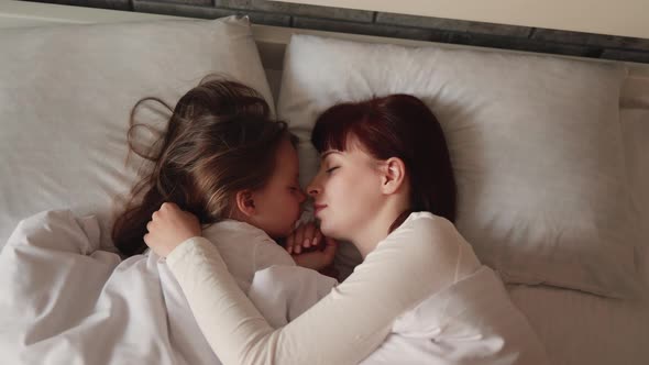 Cute Little Girl Sleeping with Her Beautiful Young Caucasian Mother in White Pajamas Lying on Pillow