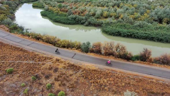 Wife waits for husband to catch up on a cycling activity on a riverside pathway - aerial view