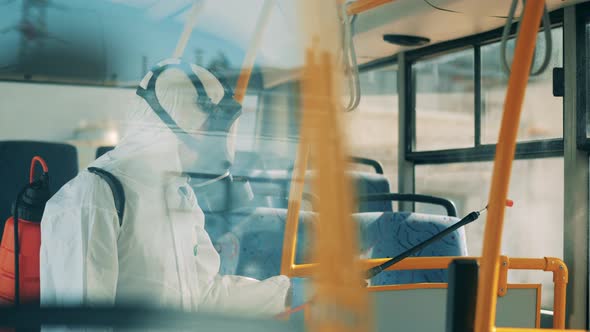 Person in Protective Suit Sprays Chemicals, Disinfectant. Bus Windows Are Getting Sanitized By a