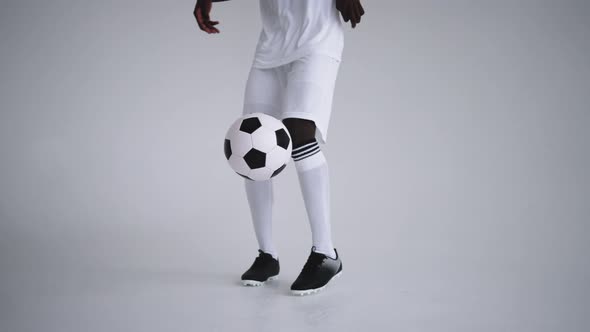 A Professional Black Football Player in a White Uniform on a White Background Juggles a Ball in Slow