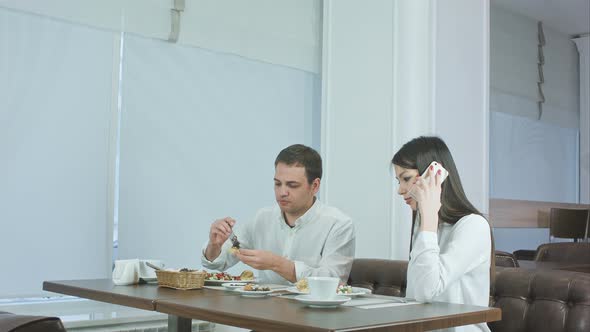 Young Man Eating While His Girlfriend Talking on the Phone at Restaurant