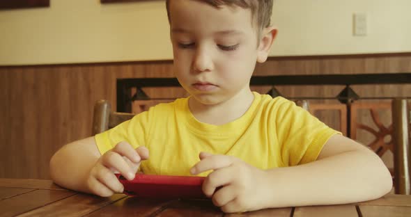 Portrait of a Child Looking at the Phone Sitting at the Table a Preschool Kid Uses Artificial