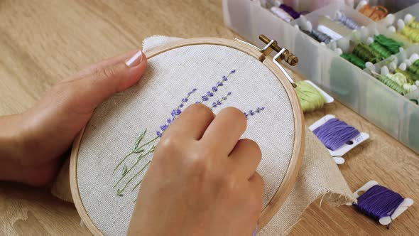 Woman embroiders very beautiful lavender flowers on linen fabric. Handmade embroidery, art, woman