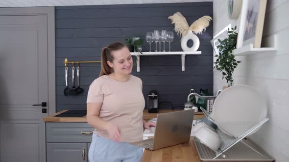 Woman Stands in the Kitchen and Communicates Via Video on Laptop