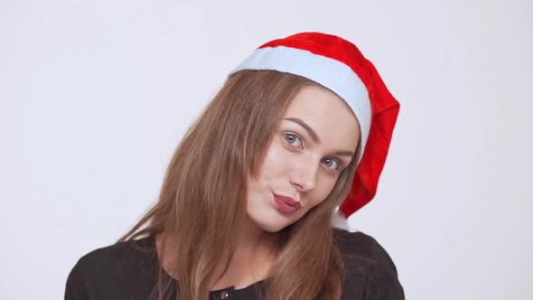 Young Beautiful Fairhaired Girl in Christmas Hat Smiling Winking Sending Kisses Ovwer White