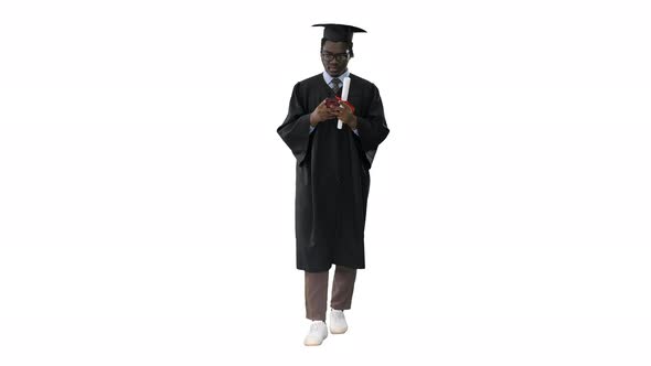 African American Male Student in Graduation Robe Texting on the Phone While Walking with His Diploma