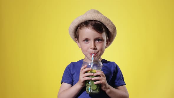 Cute boy Drinking Mojito cocktail From Plastic Cup Over Yellow Studio Background