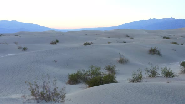 Flying over sand dunes while sun hiding behind mountains in the background. Sunset. Death Valley Nat