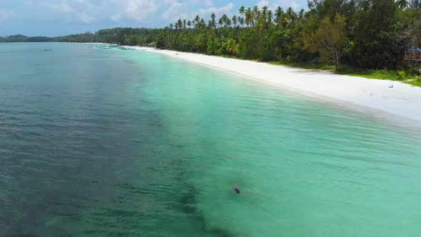 Aerial: woman swimming in turquoise water at sunset white sand beach tropical co