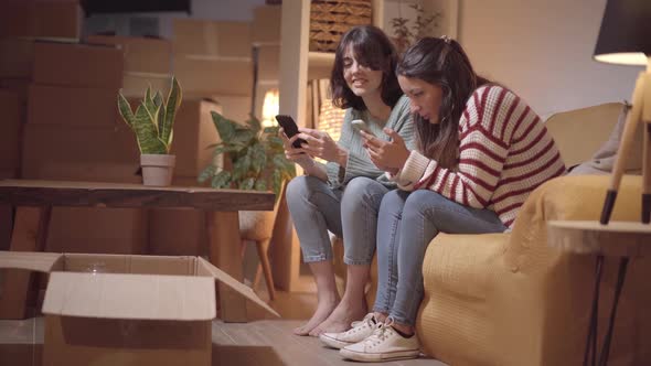 Happy Couple of Female Friends Female Landlord Tenants Sit on Sofa Use the Smart Phone on Moving Day