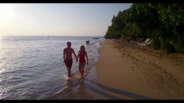 Family of two sunbathe on idyllic tourist beach adventure by clear ocean with white sandy background