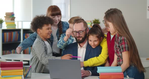 Multiethnic Preteen Children Hugging Male Teacher in Classroom