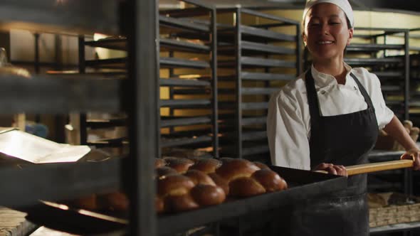 Animation of happy asian female baker holding wooden spatula with challah