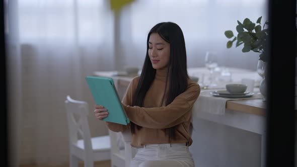 Middle Shot of Confident Slim Charming Asian Woman Surfing Internet on Tablet in Home Office Smiling