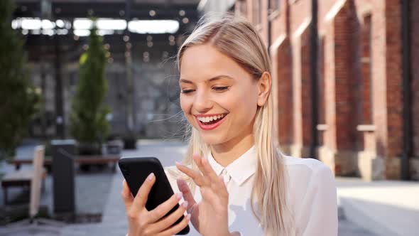 Positive Young Woman Uses Mobile Phone Chatting with Friend in Social Media