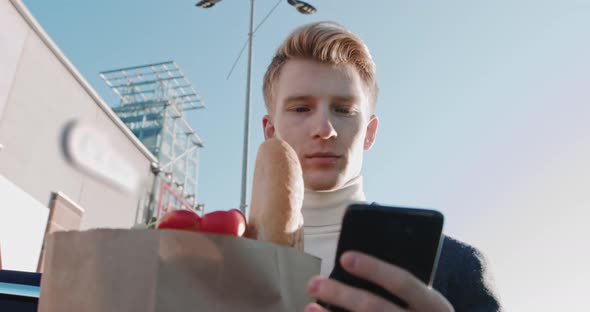 Young Handsome Guy Holds A Food Package Looks At The Phone Typing A Message