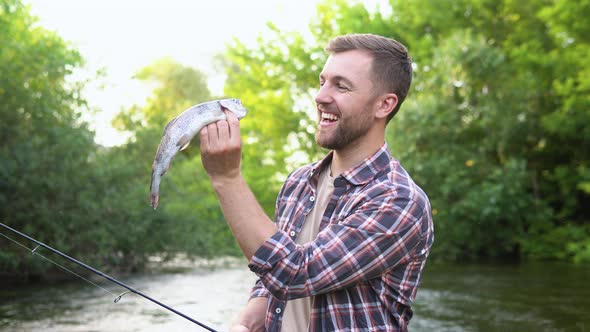 Fisherman Rests on the River and Catches Trout Smiles and Shows the Fish in the Camera