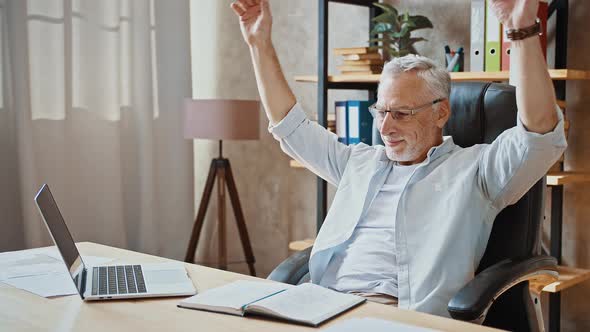 Mature Businessman Putting Hands Behind His Head and Smiling Being Happy Sitting at Table with