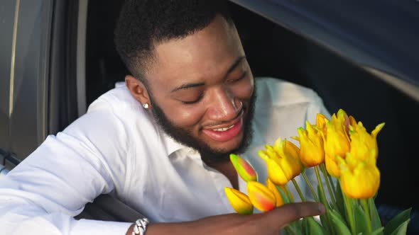 Portrait of Romantic Happy African American LGBT Man Admiring Yellow Tulips Sitting in Right Hand