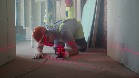 Builder Adjusting Laser Level on Floor Before Measure