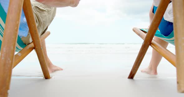 Mid section of couple holding hands on sun lounger at beach on a sunny day 4k