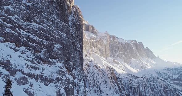 Forward Aerial Along Snowy Alpine Steep Rocky Cliff Valley