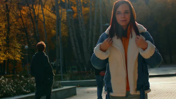 A Beautiful Woman in a Warm Denim Jacket Straightens Her Hair in an Autumn Park