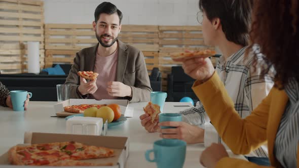 Happy Middle Eastern Man Talking To Caucasian Women Colleagues Eating Pizza at Corporate Party