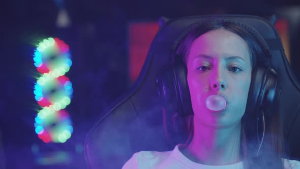 Young Gamer Woman Sitting in a Chair in Gaming Club and Blowing a Bubble Gum in the Room Filled